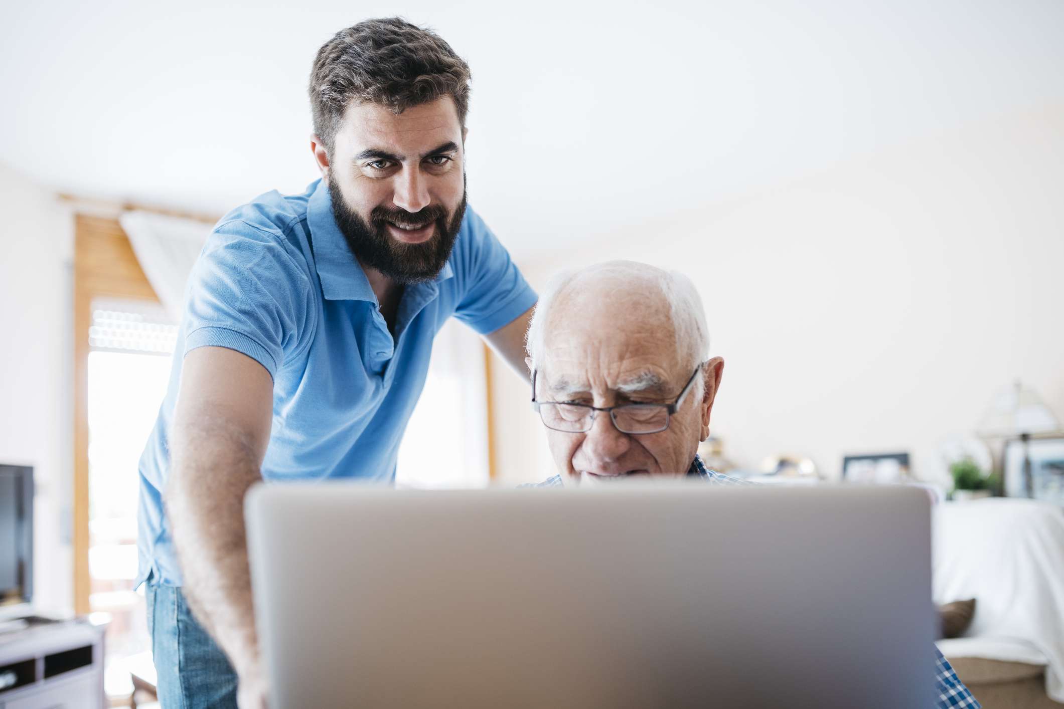 Mladší dospělý pomáhá staršímu dospělému u počítače. 