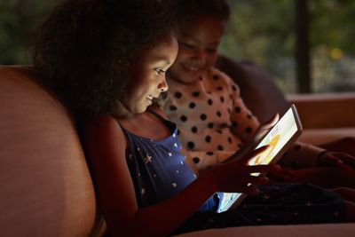 Dvě mladé dívky hrající na digitálním tabletu, v noci.