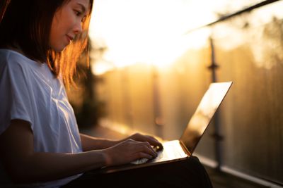 Žena sedí při pohledu na svůj notebook v tlumeném osvětlení venku