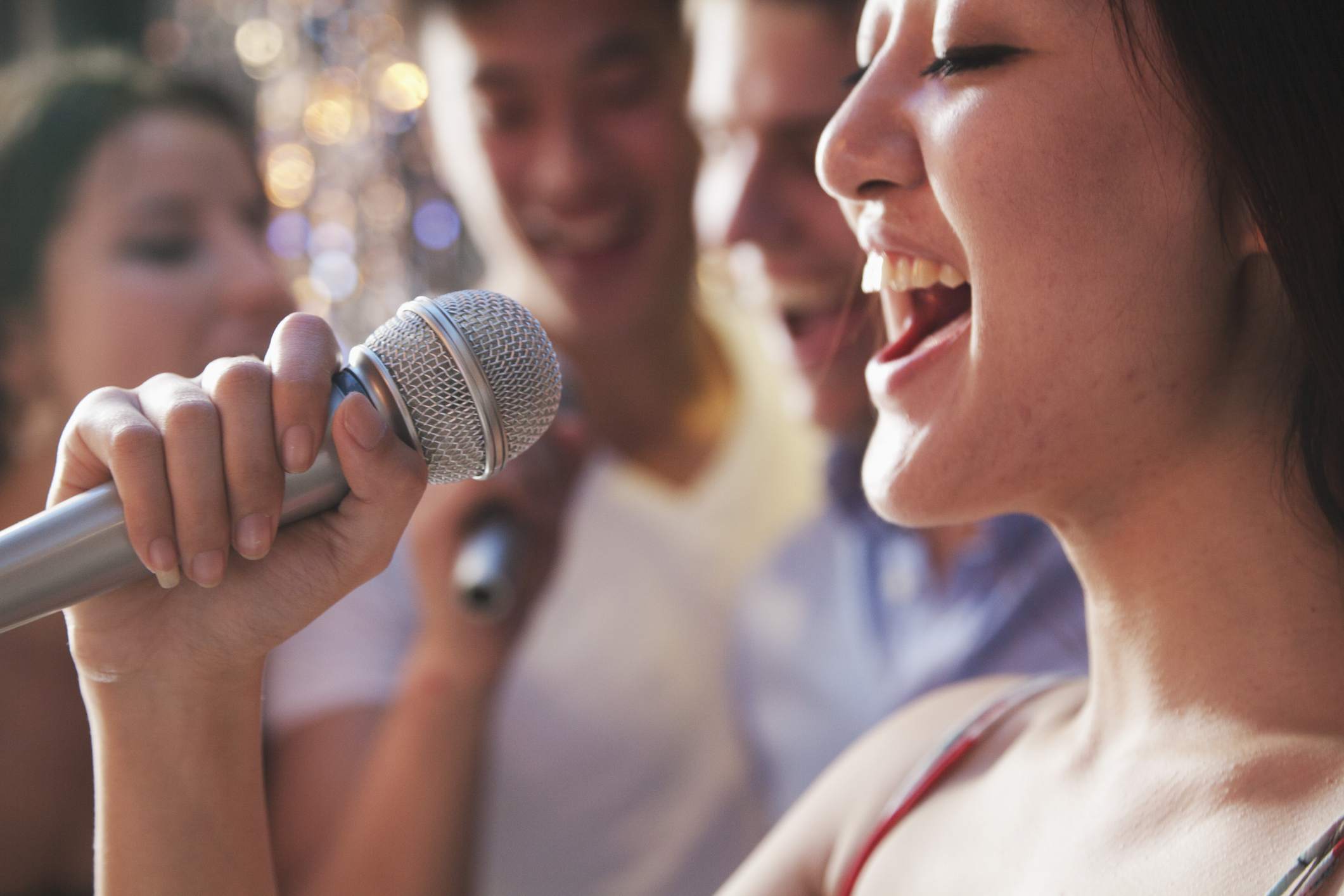 Detailní záběr na ženu zpívající do mikrofonu s přáteli v pozadí