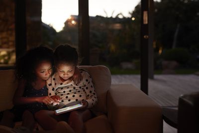 Žena a její dítě sedí ve tmě na gauči a dívají se na přenosné herní zařízení