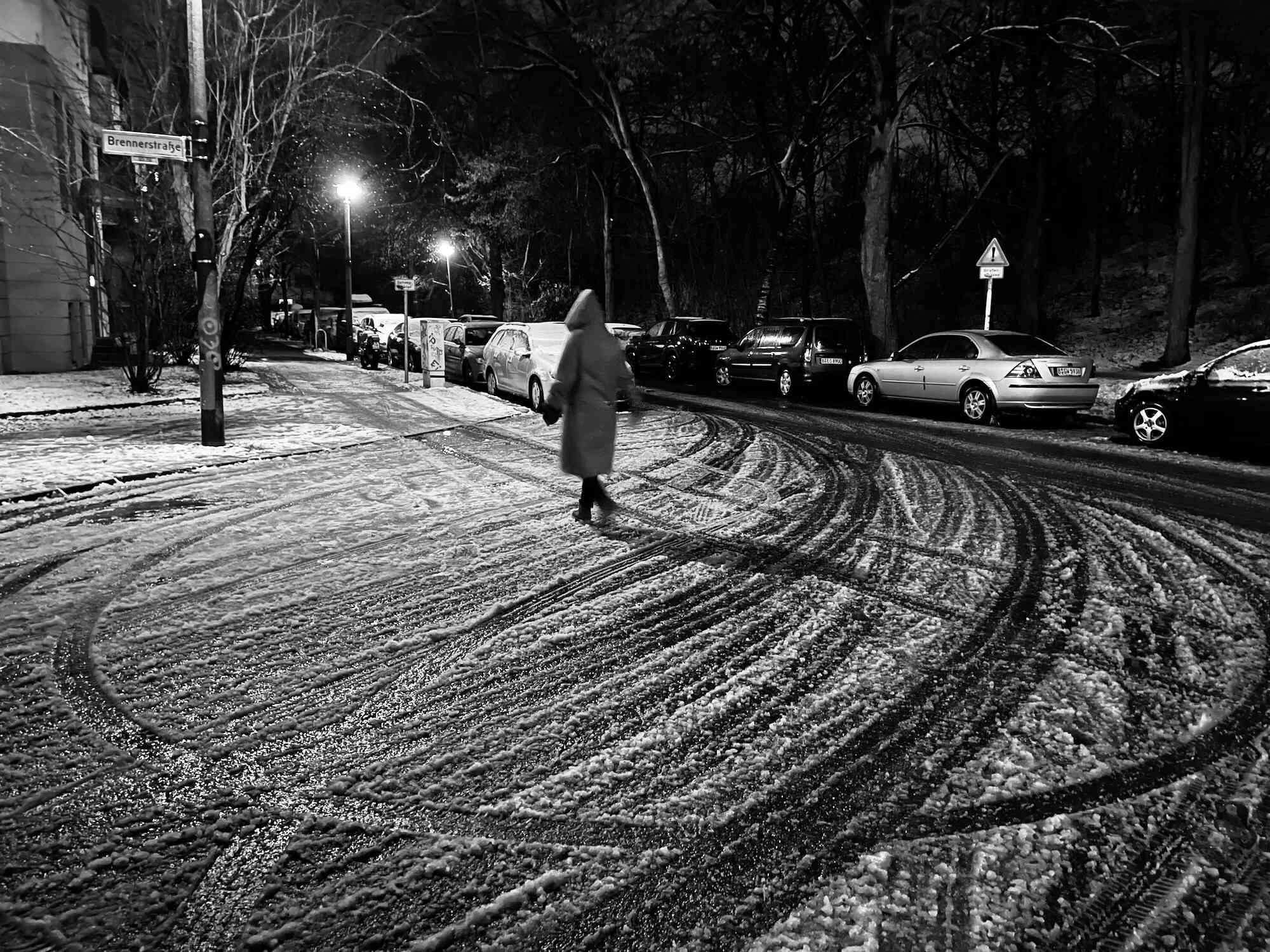 Obrázek pro mini kameru iPhone 12 zobrazující osobu, která kráčí v zasněžené noci s auty zaparkovanými na ulici.