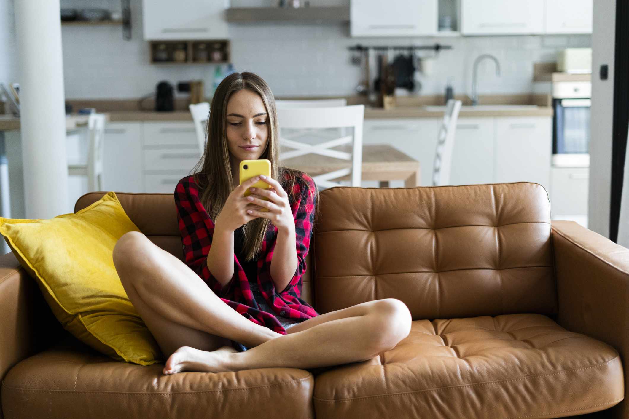 Mladý člověk pomocí smartphonu, zatímco sedí na gauči doma.