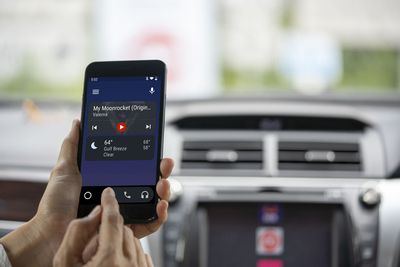 Řidič, který drží telefon se systémem Android Auto v autě.