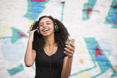 Osoba poslouchající mobilní telefon s kabelovými sluchátky a usmívá se