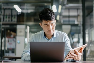 Muž sedí u stolu a současně se dívá na notebook a tablet