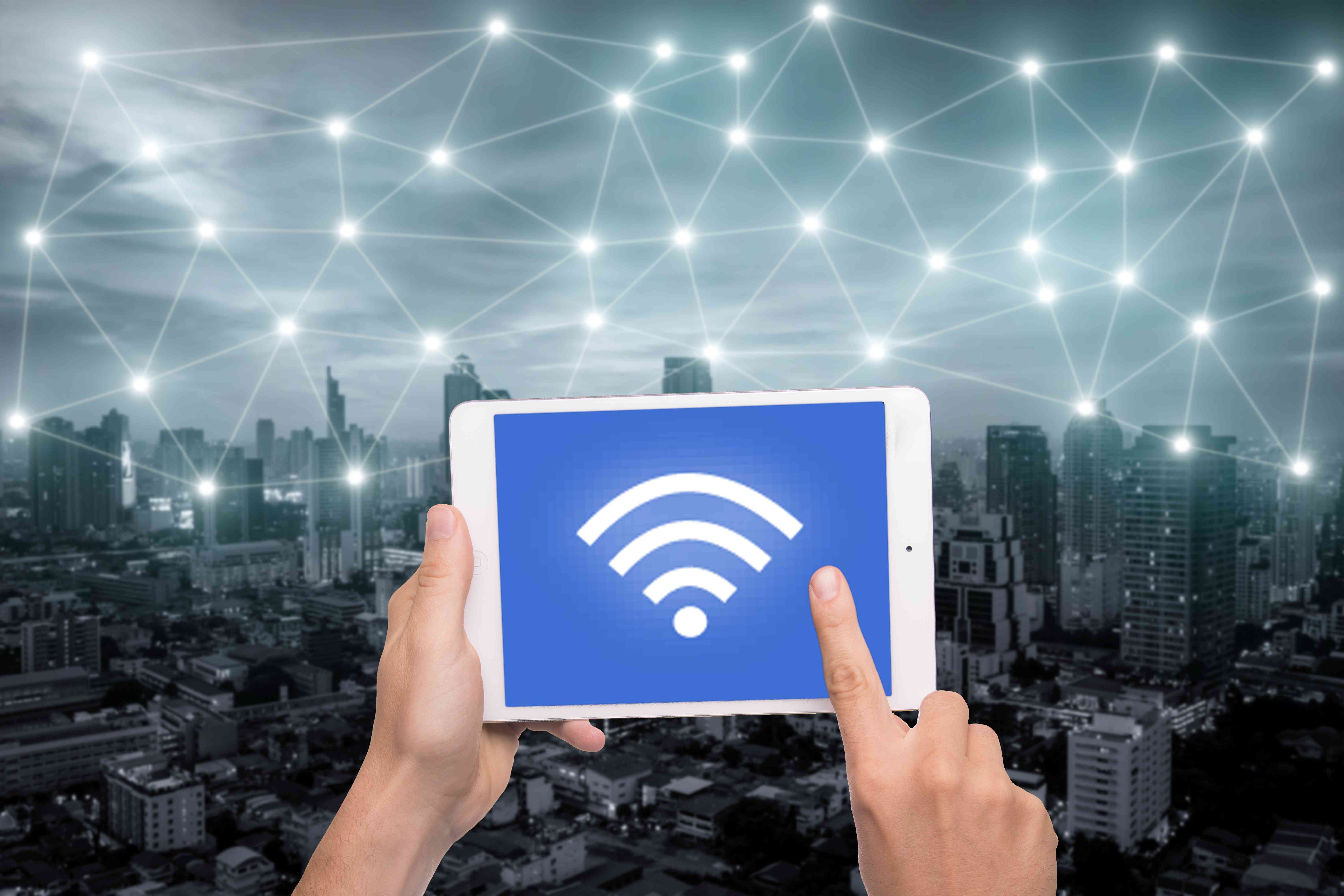 Ruka držící tablet s ikonou Wi-Fi na konceptu připojení k městu a síti.