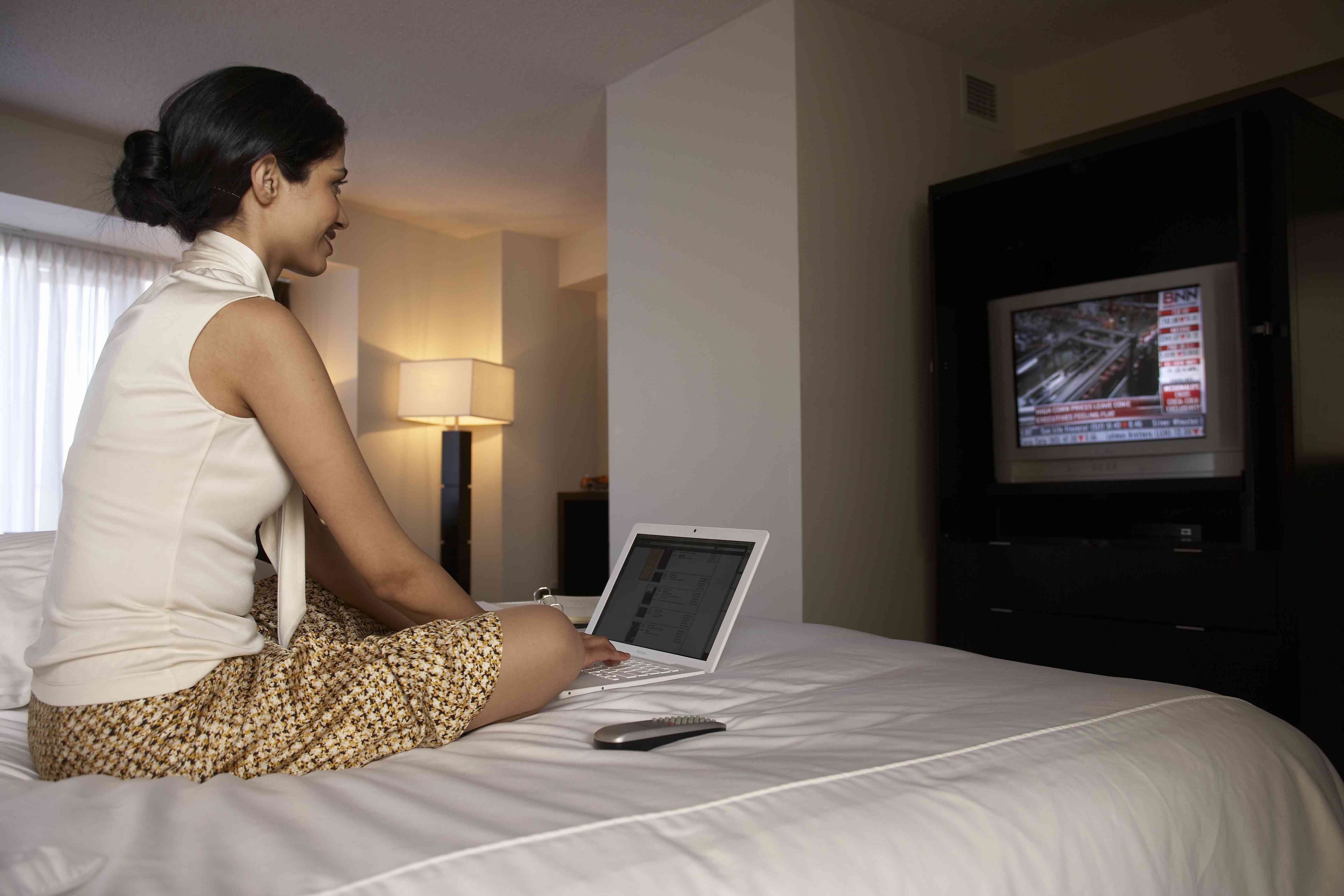 Žena na hotelové posteli s notebookem sledovat finanční zprávy