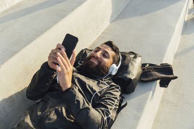 Muž leží na zádech, poslouchá sluchátka a pomocí iphone