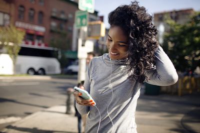 Žena při pohledu na její iPhone a pomocí sluchátek na ulici ve městě