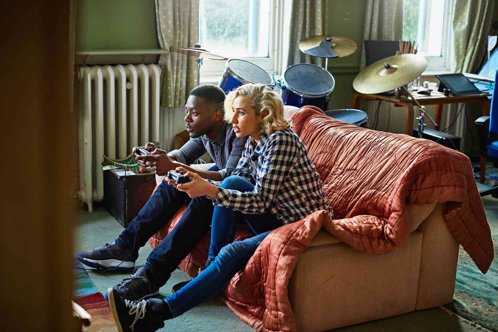 Dva mladí dospělí hrající konzolové videohry sedí na gauči v malém bytě.