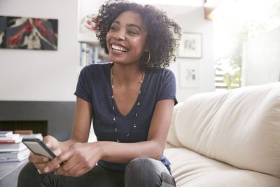 S úsměvem afroamerické ženy s mobilním telefonem na pohovce v obývacím pokoji