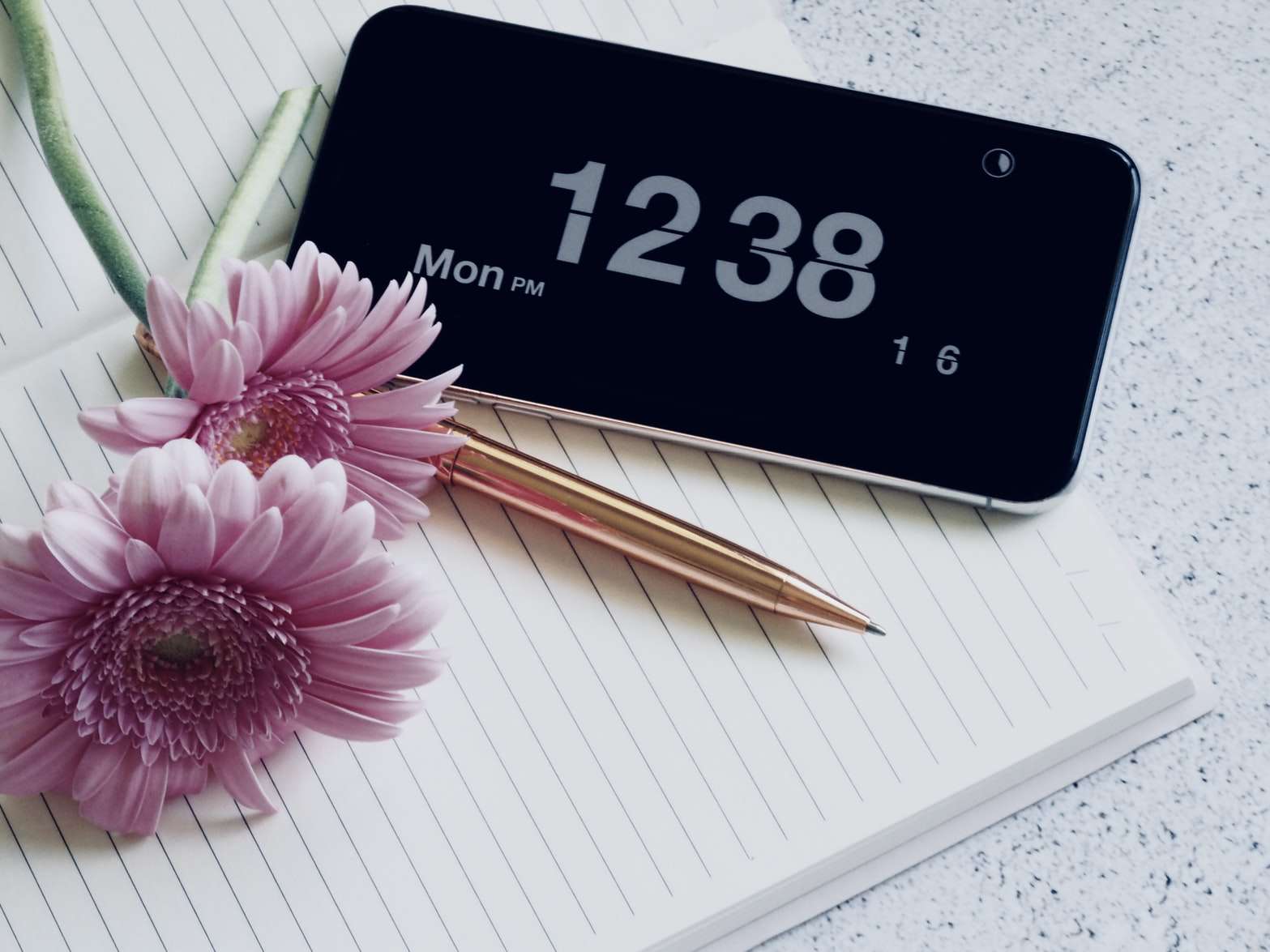 iPhone ukazuje čas při odpočinku na notebooku s perem