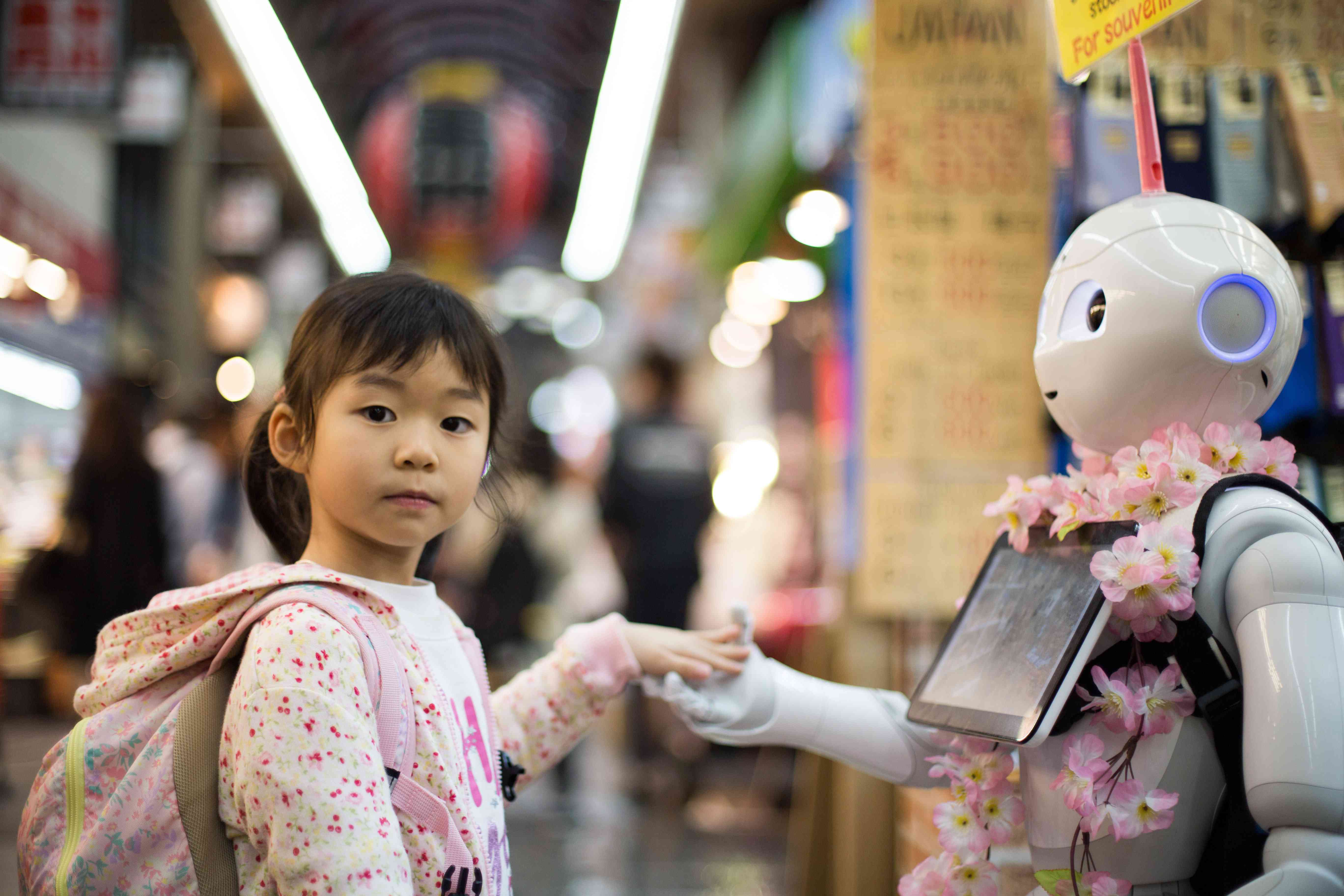 Dítě drží ruku robota na rušném trhu.