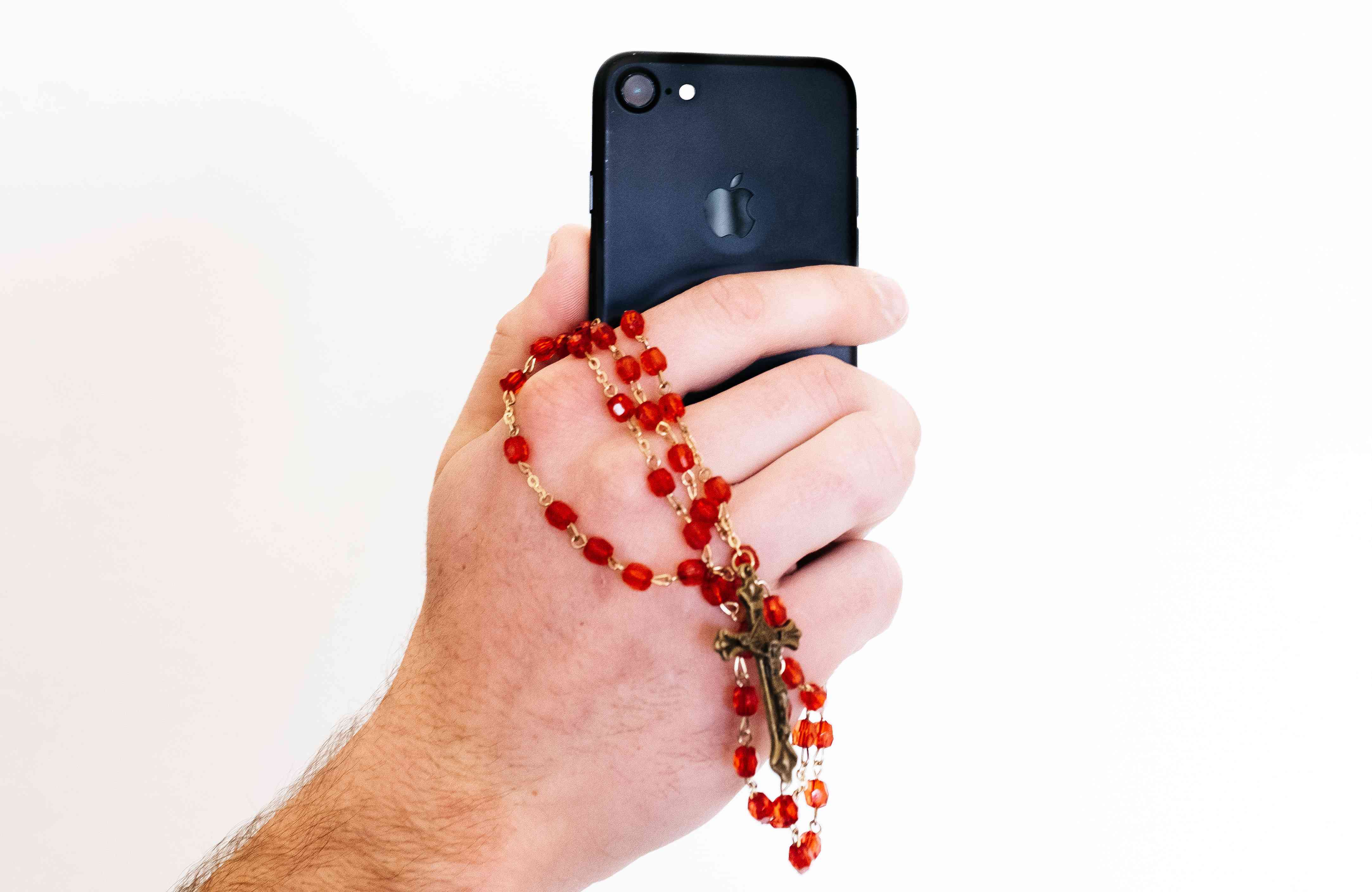 Detail ruky držící smartphone a růženec.