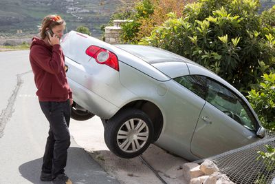 Osoba na mobilním telefonu vedle automobilu, který sjel ze silnice.