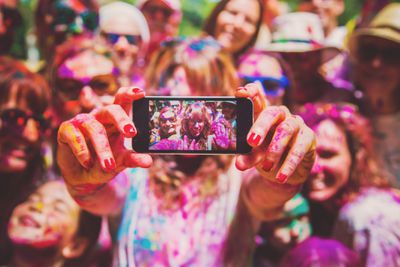 Lidé pokrytí barvou si pořizují selfie na iPhonu