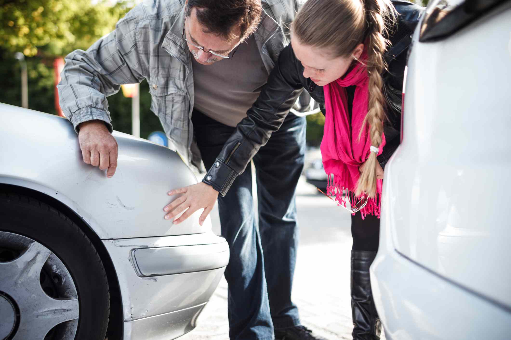 Detail muže a mladší ženy zkoumající auto po nehodě.