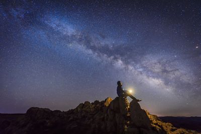 Osoba sedící pod galaxií Mléčná dráha se světlem na rukou.