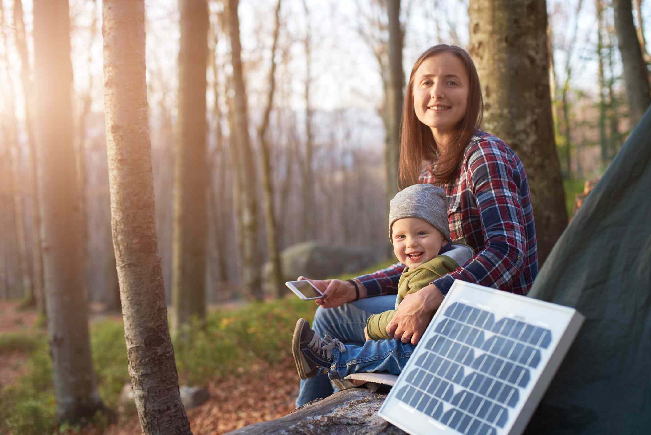 Mladý rodič a dítě poblíž stanu v lese se solárním panelem, který získává energii ze slunce.