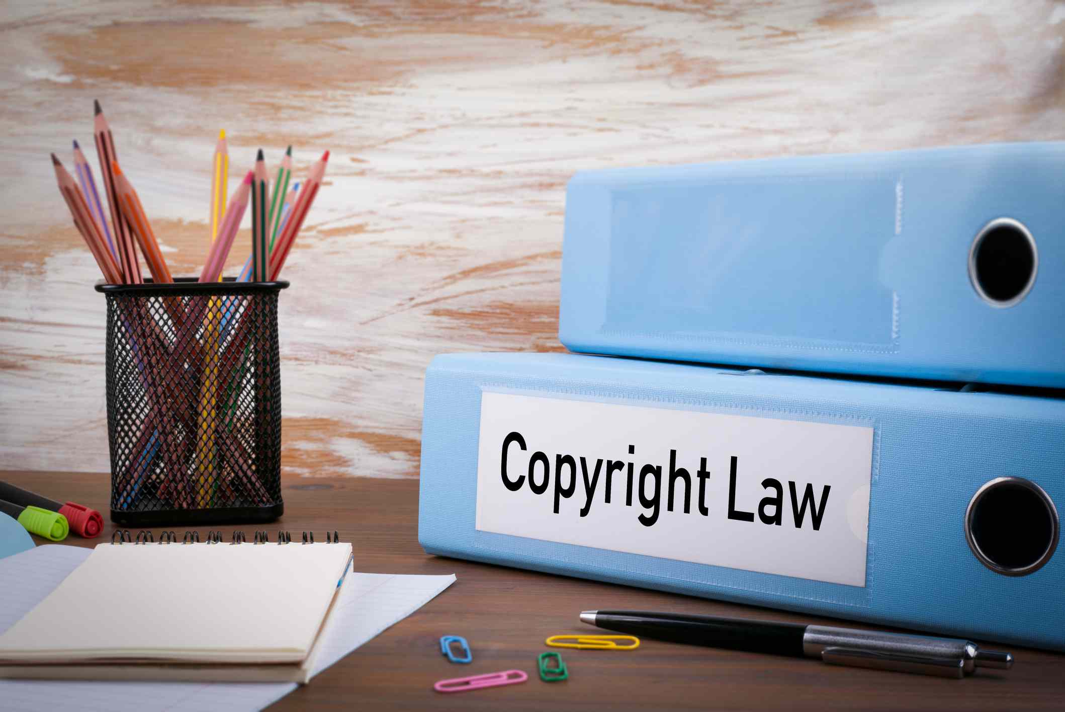 Pořadač označený jako „autorský zákon“ sedí na stole s poznámkovými bloky, kancelářskými sponkami a psacími nástroji.