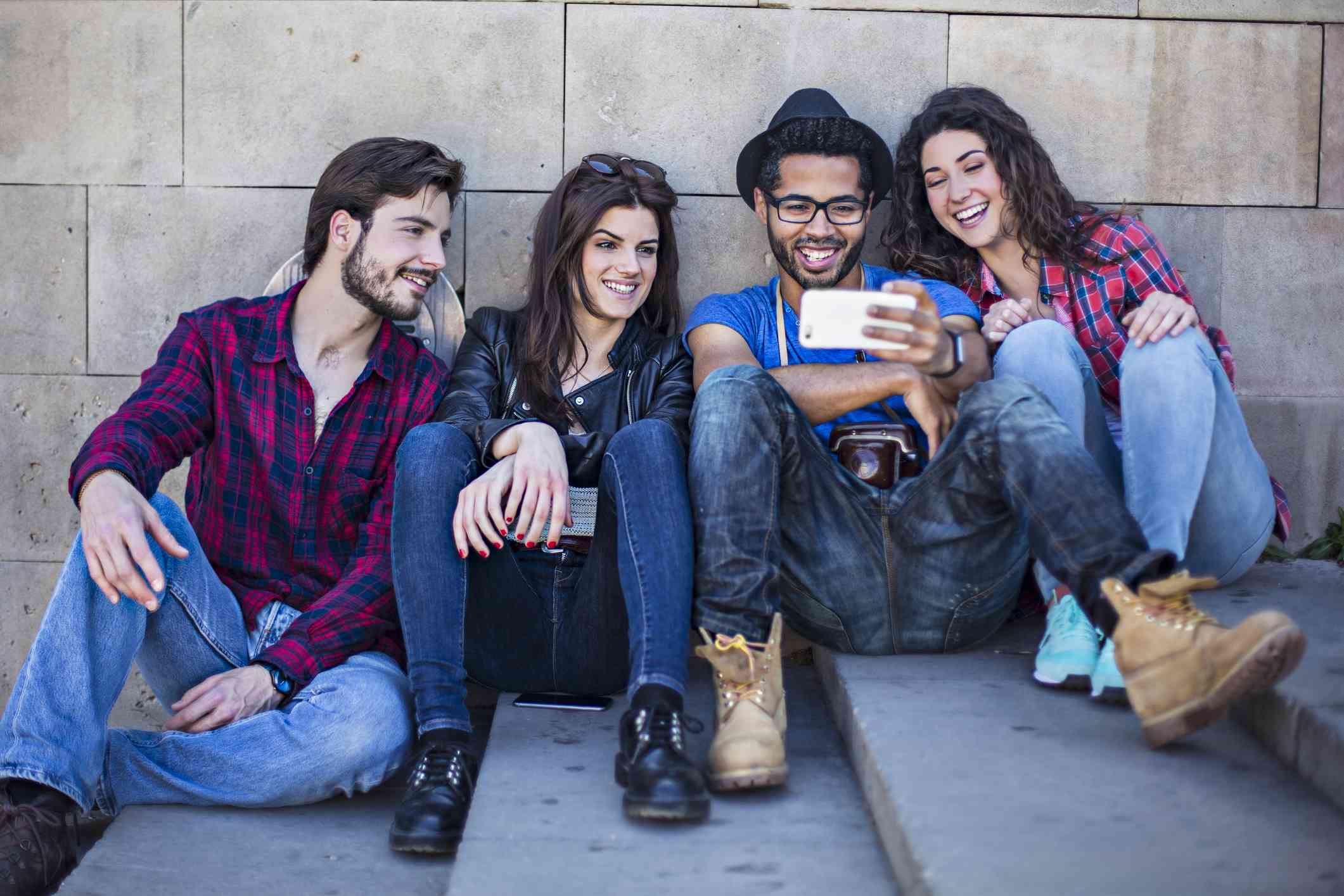 Čtyři přátelé sledují film na smartphonu sedí venku na betonových schodech.