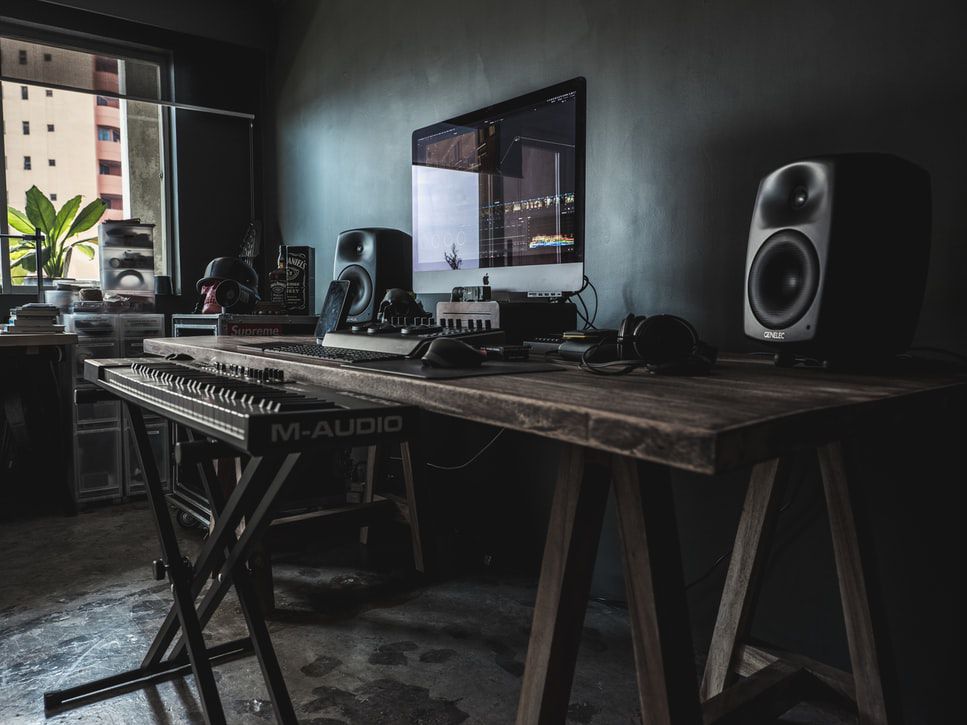 Hnědý dřevěný stůl s počítačem Mac a před ním stojící hudební klávesnice.