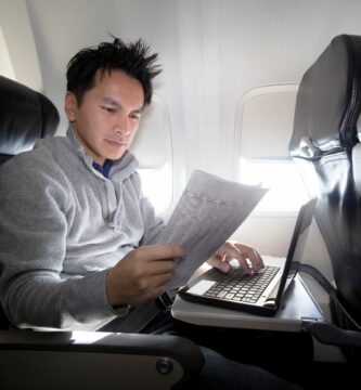 YoungAsianmanusinglaptopandreadingnewspaperonplane 59960904685fbe00103478bd