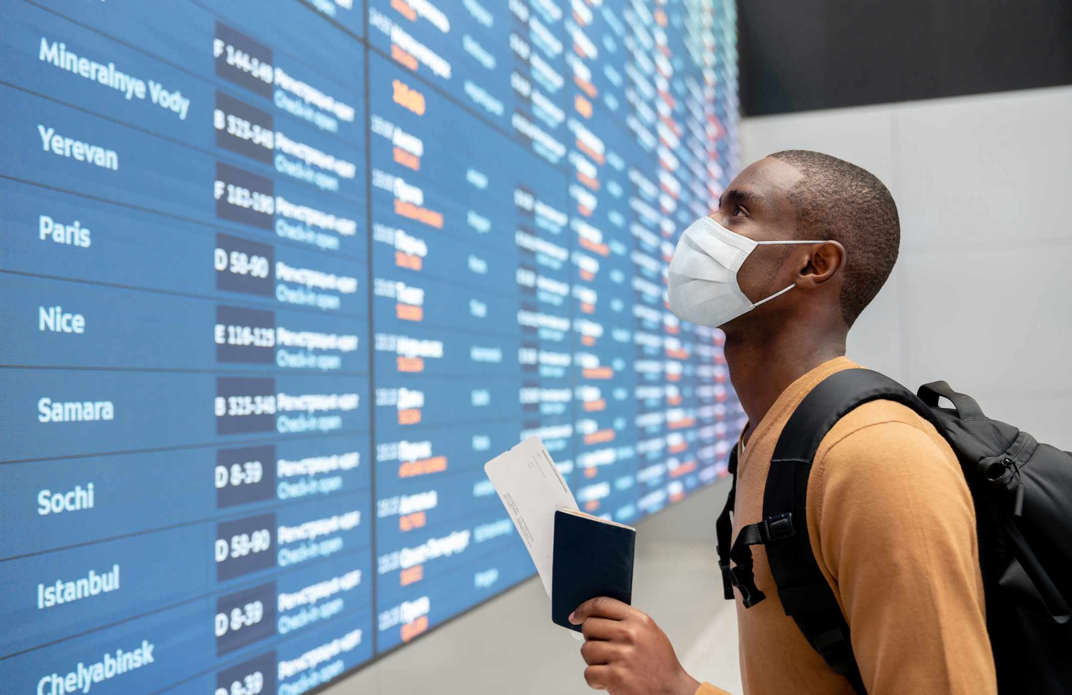 Cestující na obličeji s maskou na letišti a při pohledu na letový řád.