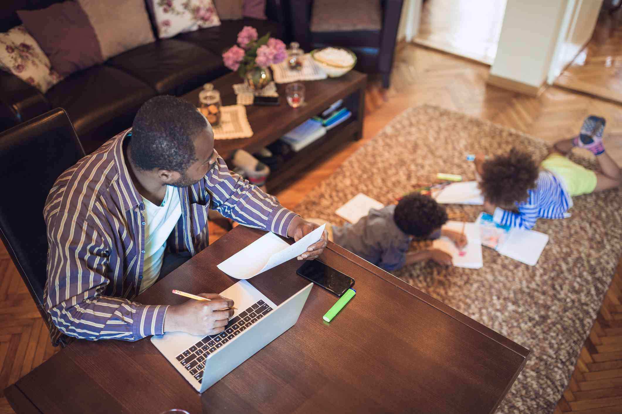 Otec pracuje z domova, zatímco jeho dvě děti si hrají v obývacím pokoji