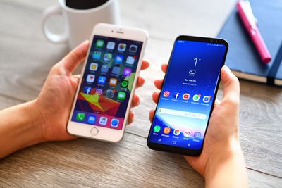 Telefon iPhone a Samsung držený vedle sebe na stole