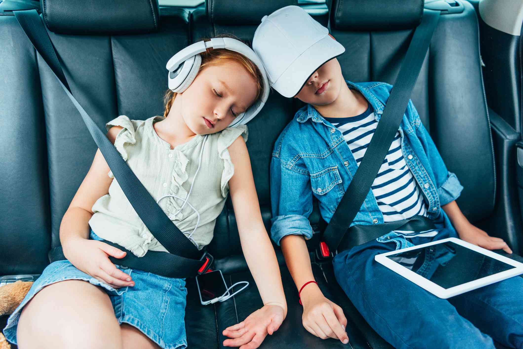 Dvě děti spí v autě a drží elektronická zařízení, která lze použít pro školní práci. 