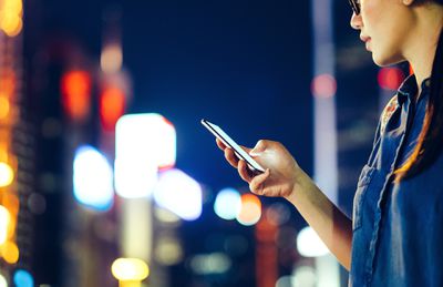 Žena na ulici v noci při pohledu na její smartphone.