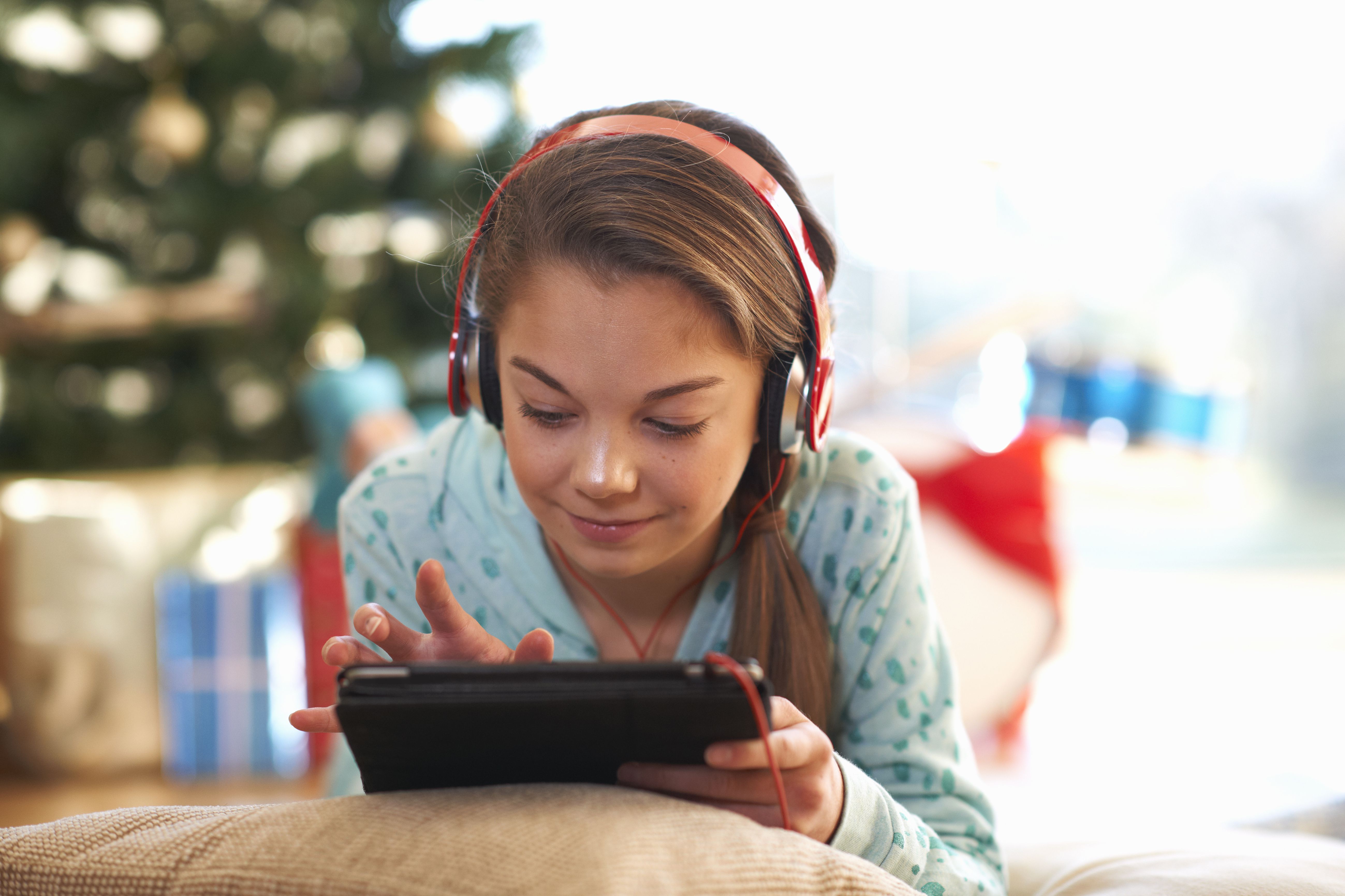 Dívka ležela na podlaze obývacího pokoje pomocí digitálního tabletu dotykový displej o Vánocích