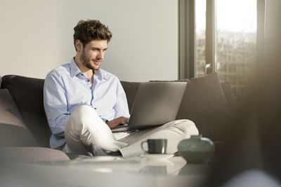 Telecommuter sedí na gauči doma pomocí přenosného počítače