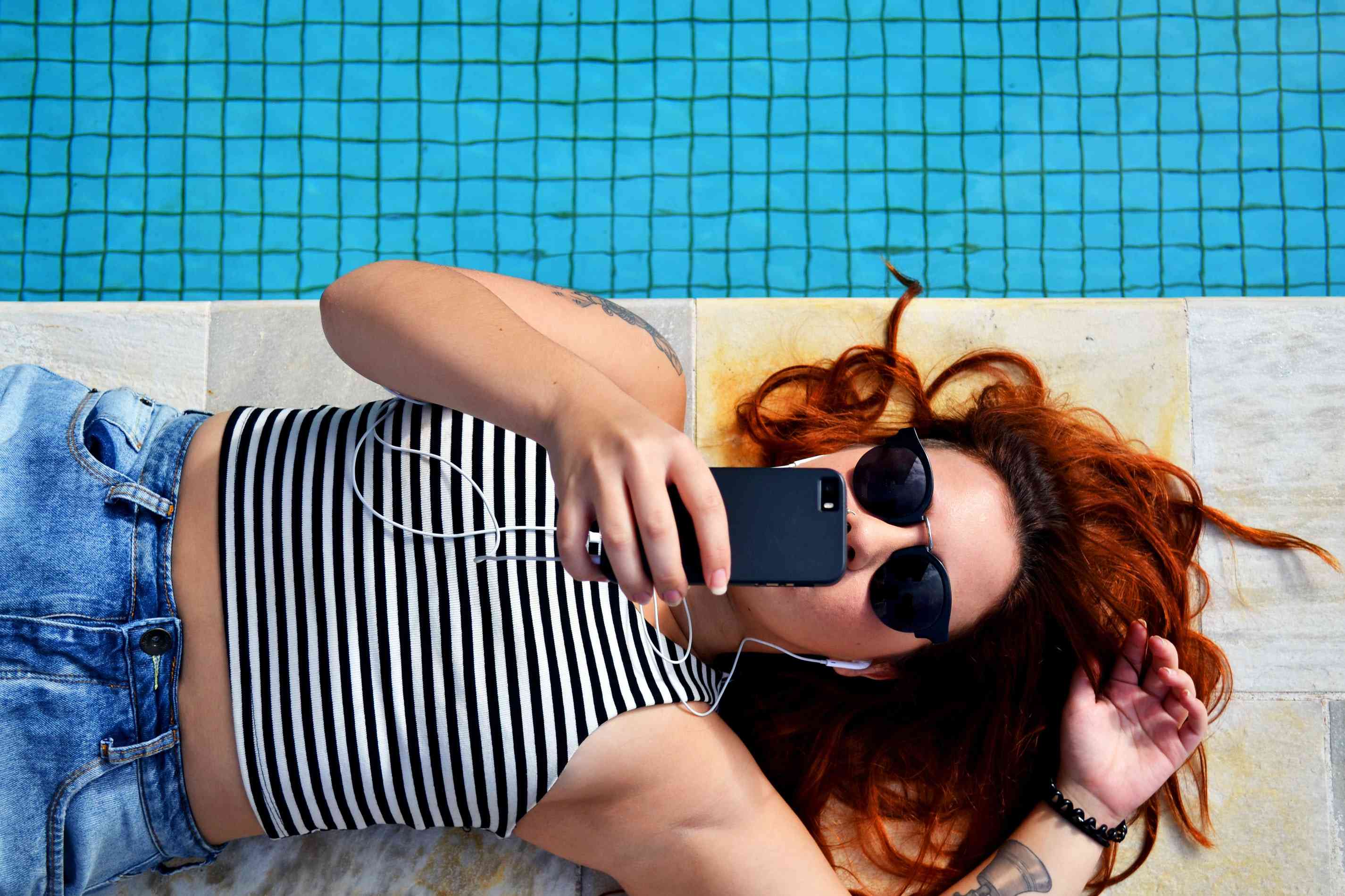 Žena leží vedle bazénu a poslouchá jejich telefon