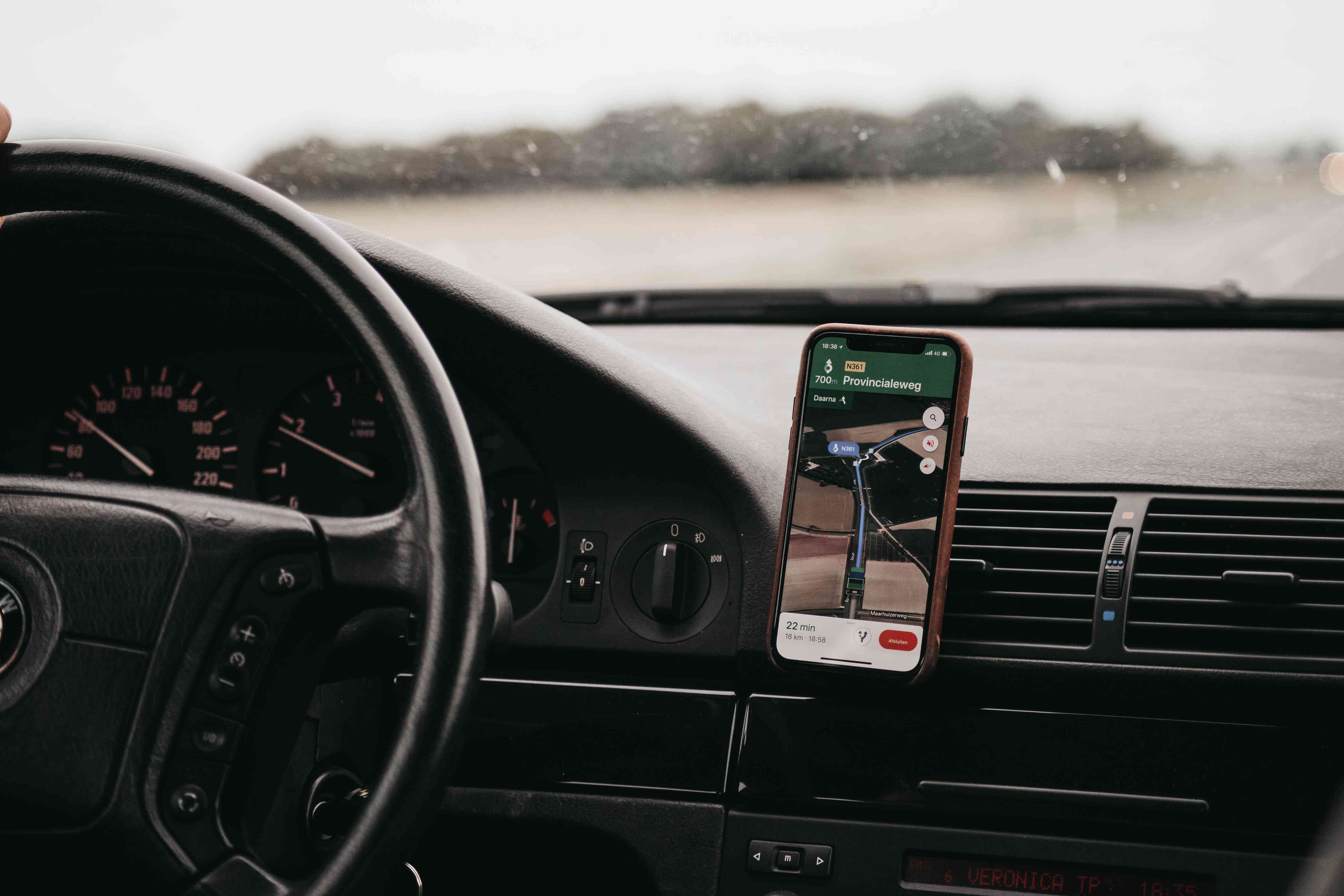 Smartphone namontovaný na větracím otvoru automobilu zobrazující mapovací aplikaci. 