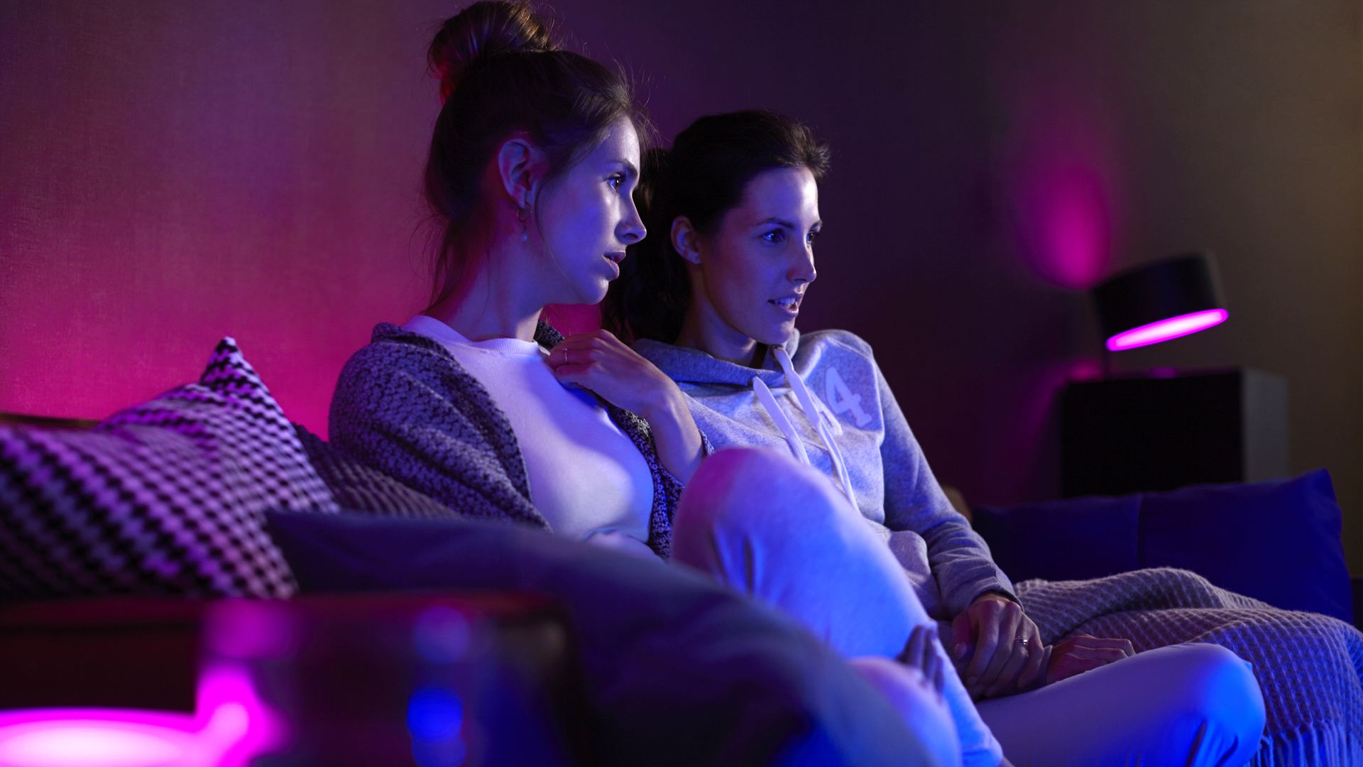 Dvě ženy sledující televizi s růžovými světly Philips Hue