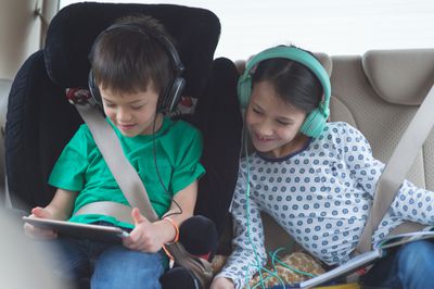 Dítě hrající hru na tabletu v autě, zatímco sestra sleduje