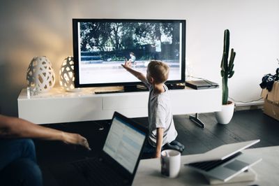 Mladý chlapec se dotýká televizní obrazovky a digitální fotografie se na ni přenáší z notebooku přes chromecast.