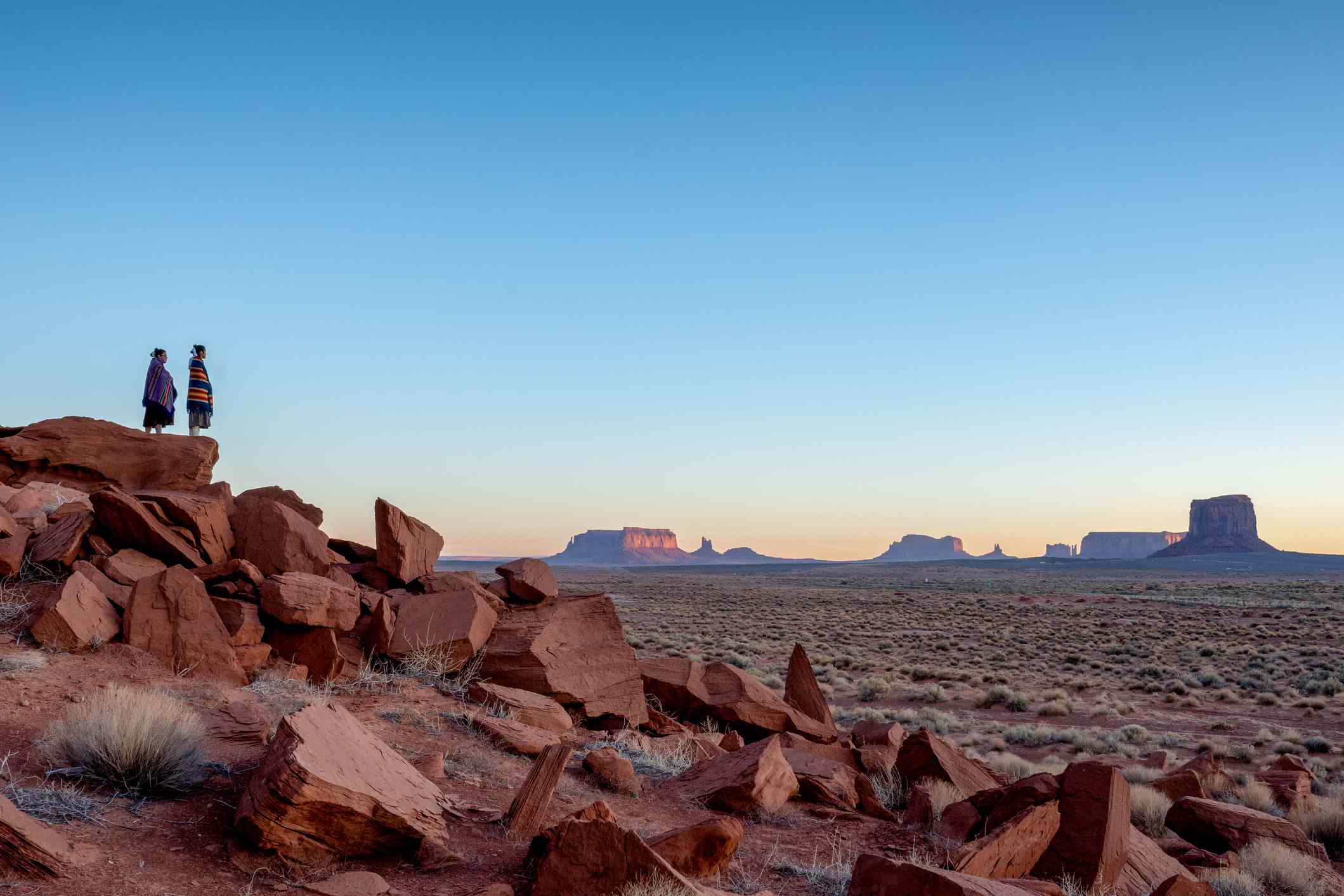 Dvě dospívající indiánské indiánské sestry Navajo v tradičním oděvu, těšící se z obrovské pouště a krajiny Red Rock ve slavném kmenovém parku Navajo v Monument Valley Arizona za úsvitu