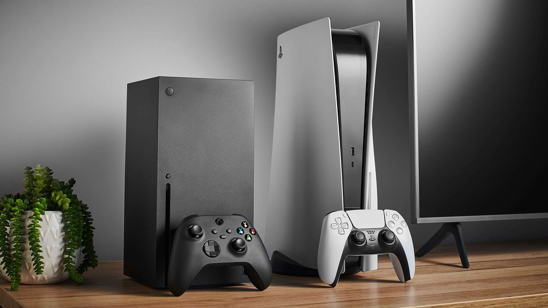 Xbox Series X a PS 5 umístěné vedle sebe v zábavním centru s televizí.