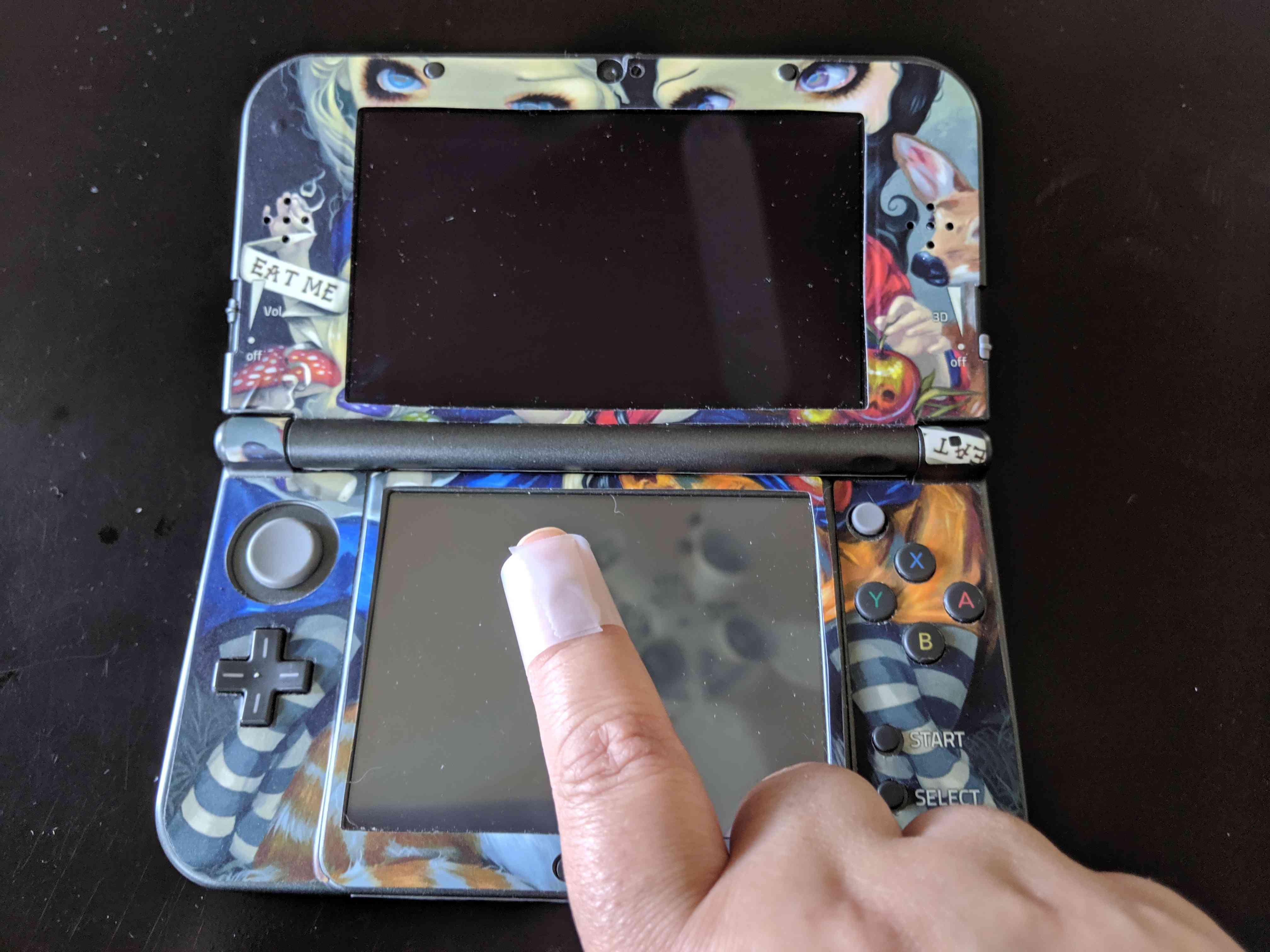 Ruka maže prach na obrazovce Nintendo 3DS se skotskou páskou