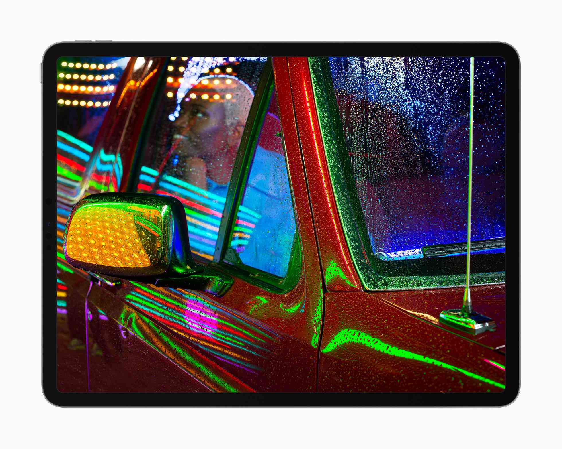 Displej Apple iPad Pro liquidXDR zobrazující fotku někoho uvnitř pickupu s neonovými světly odrážejícími se od kovu a skla.
