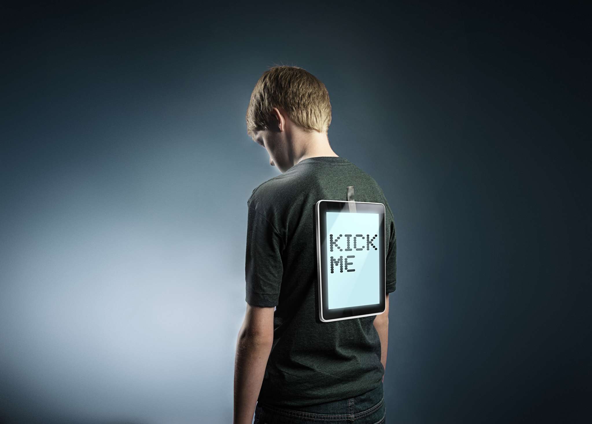 Mladý teenager s tabletem přilepeným k jejich zádům, který říká „Kick me“, představuje kyberšikanu.