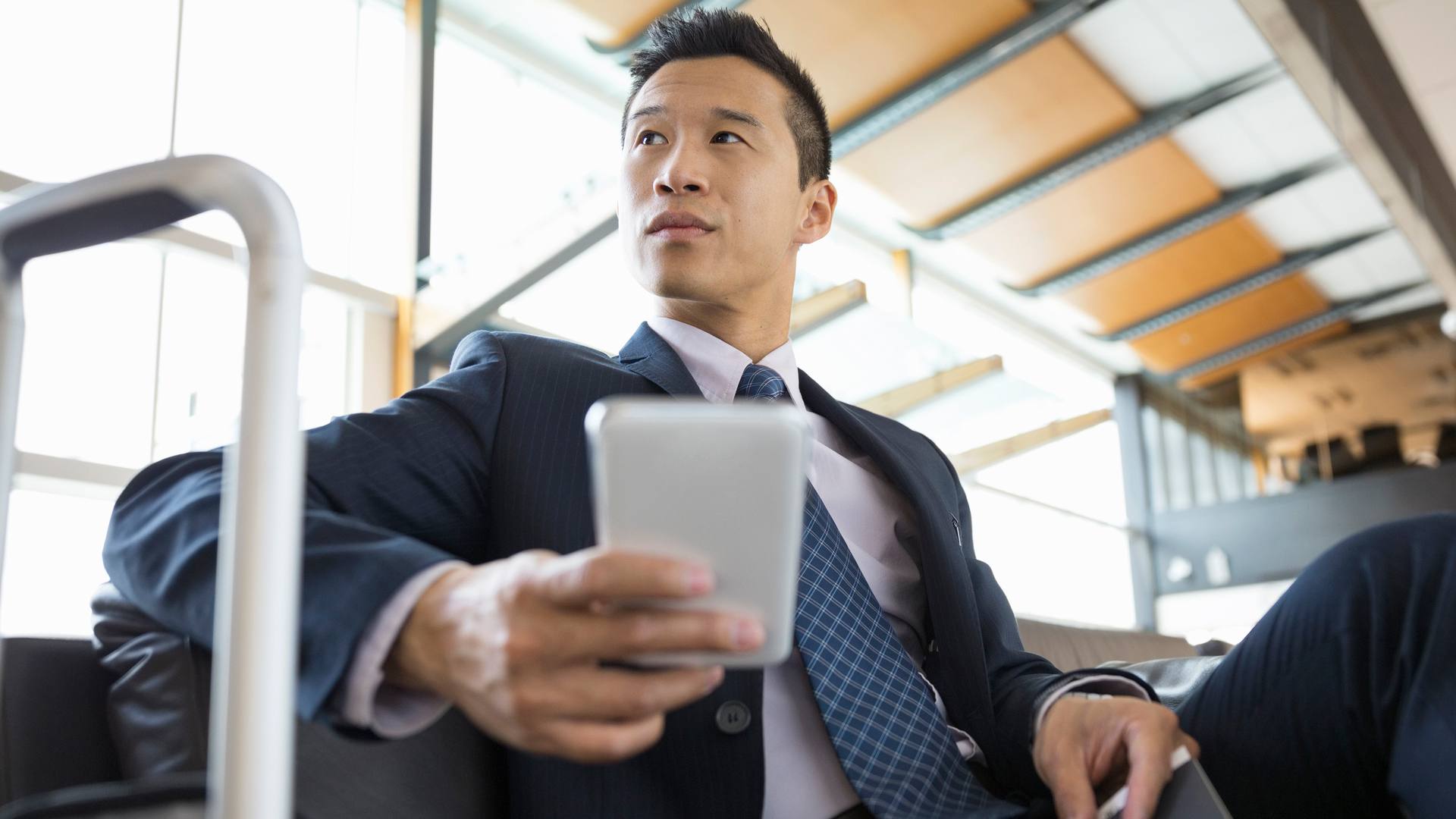 Asijský podnikatel na služební cestě, kontrola telefonu s přenosným wi-fi.