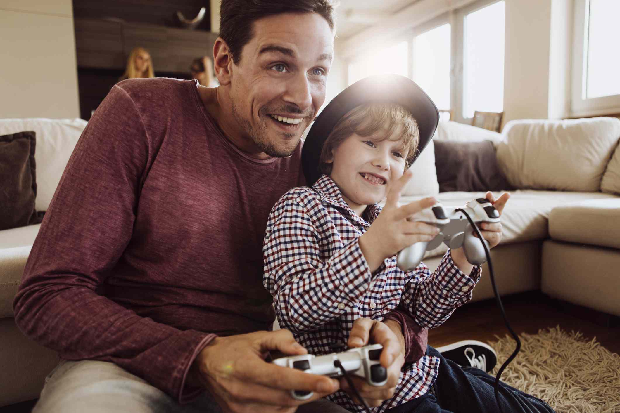 Rodič a dítě, které spolu hrají hry PlayStation, sedí na podlaze v obývacím pokoji. 