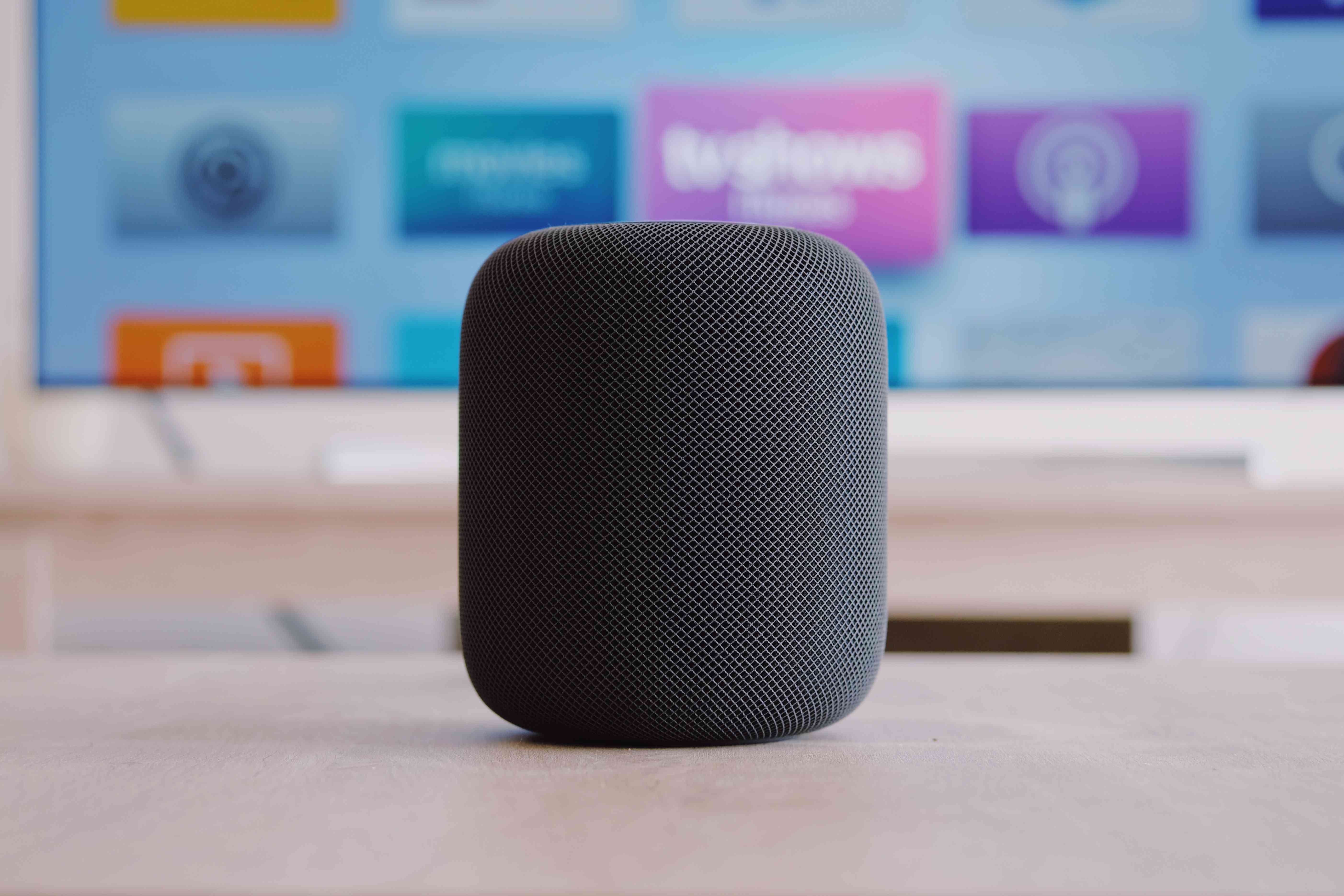 Apple Homepod s televizí v pozadí.