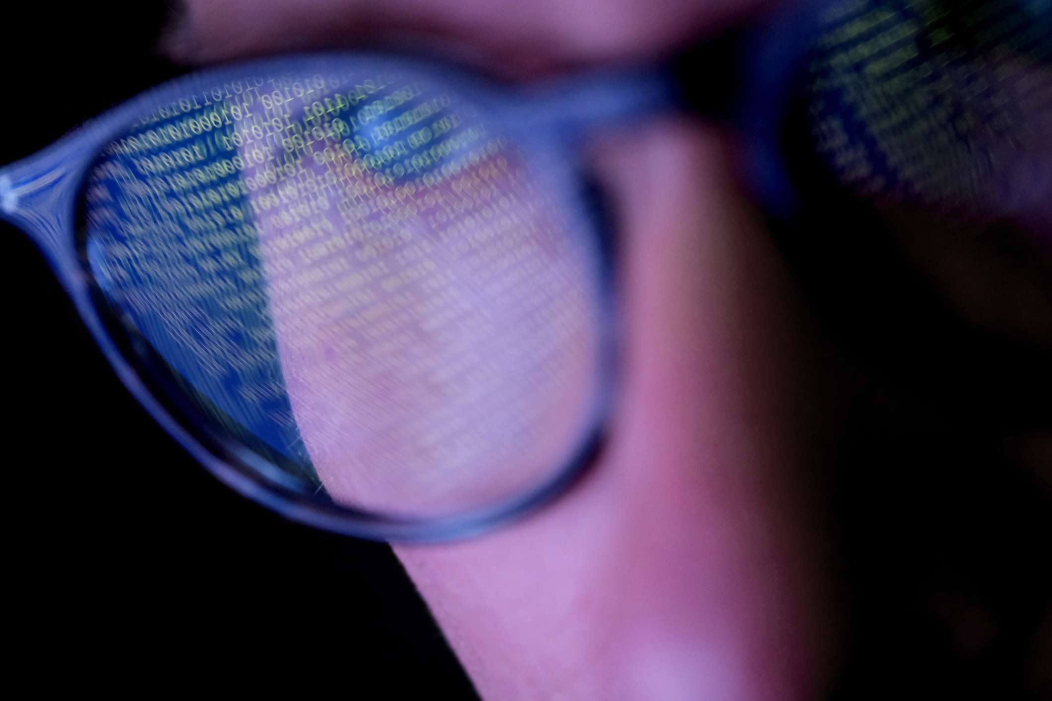 Detailní záběr na někoho, kdo nosí brýle s binárním kódem odrážejícím se na čočkách. 