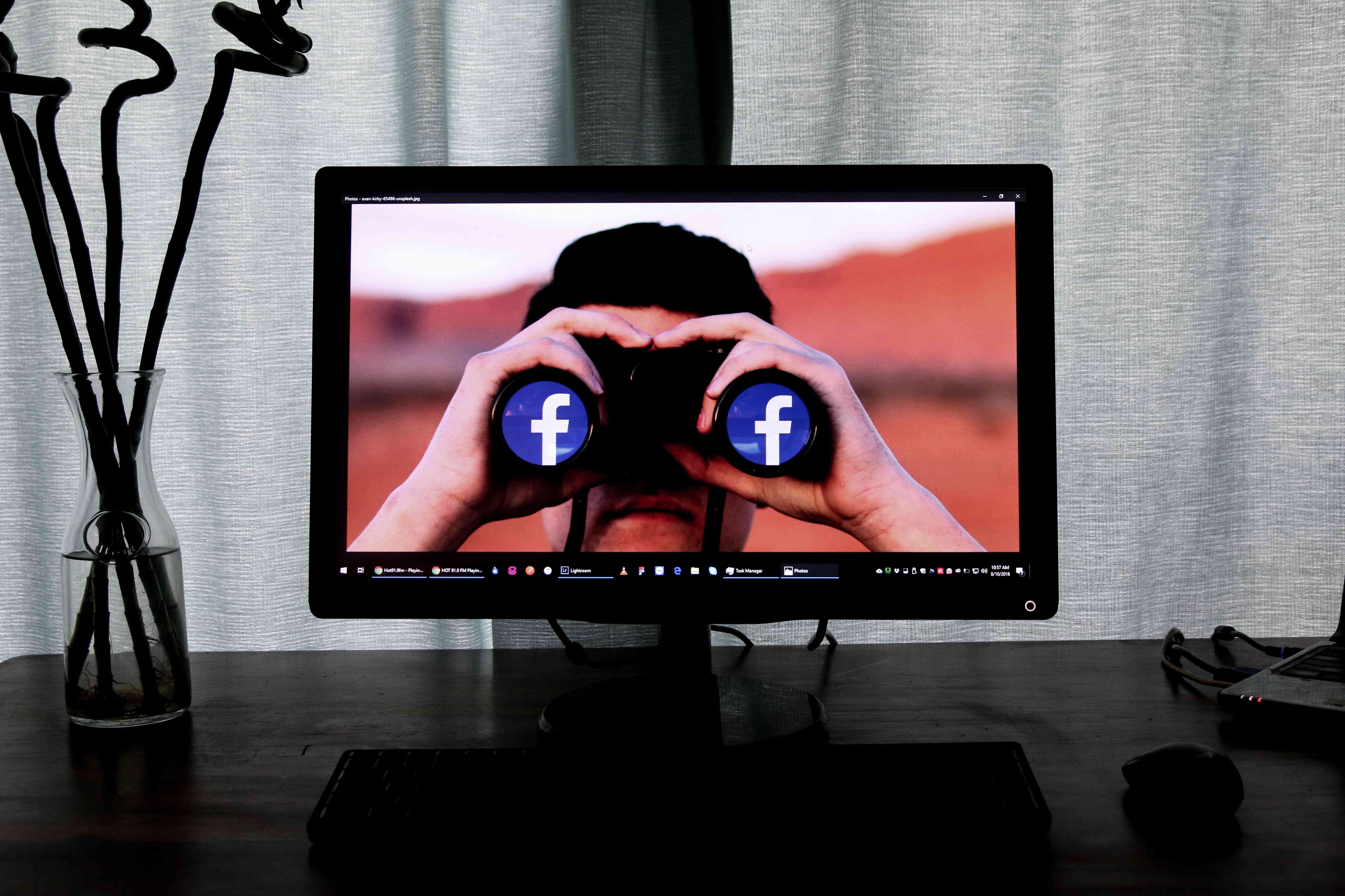 Obrazovka počítače zobrazující obrázek osoby, která drží dalekohled na tváři s logem Facebooku namísto čoček.
